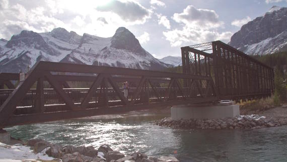 Mountainous sky scene with a steel bridge over a river, couple kissing on bridge - Mountain Wedding Videos