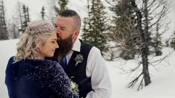 Groom kissing bride on forehead outside in snowy forest - Mountain Wedding Videos